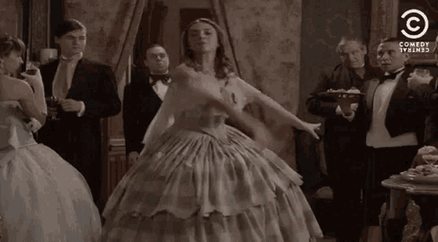 a woman in a ball gown is dancing in a room with a group of men in tuxedos .