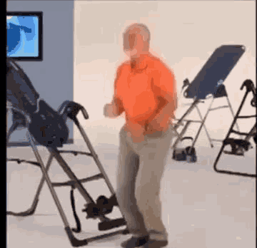 a man in an orange shirt is dancing in front of an inversion chair .