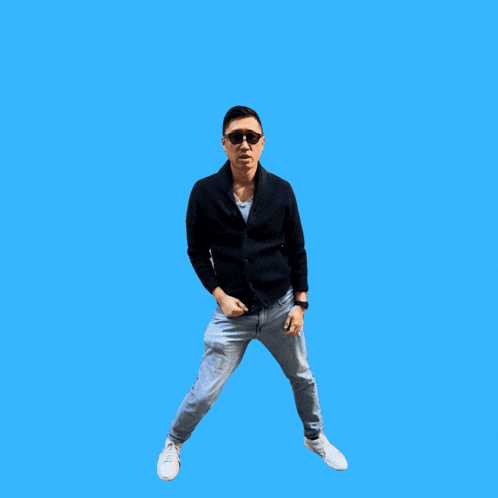 a man wearing sunglasses and a black jacket is dancing with a blue background