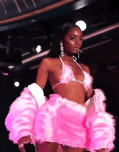 a woman is walking down a runway wearing a pink outfit with a cigarette in her mouth