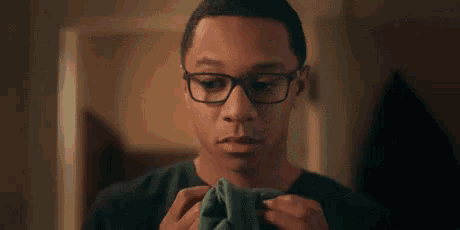 a young man wearing glasses is holding a piece of fabric in his hands .