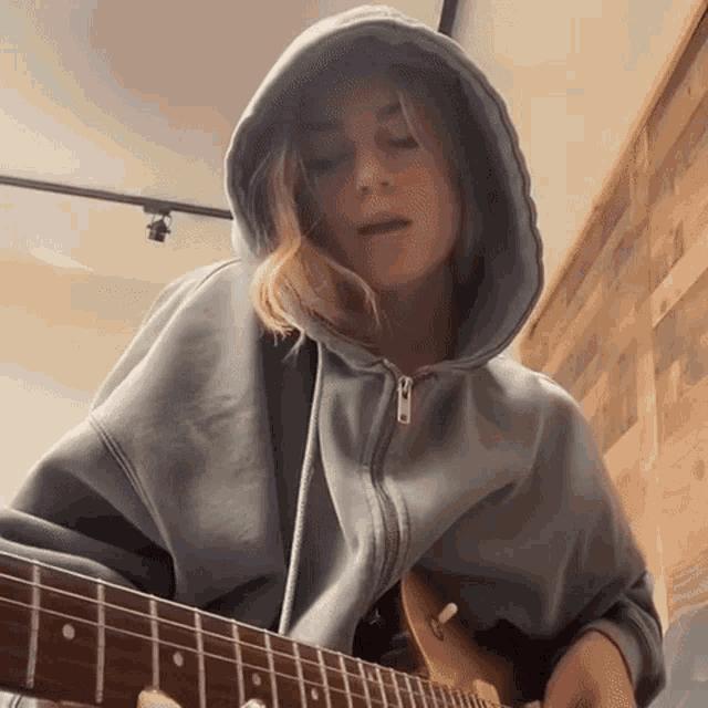 a woman in a blue hoodie is playing a guitar