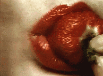 a close up of a woman 's lips with red lipstick holding a pepper .
