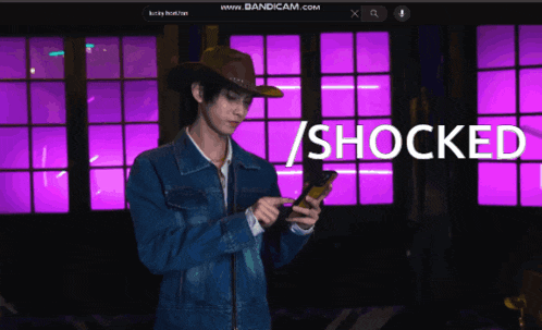 a man wearing a cowboy hat is looking at his phone with the words shocked behind him