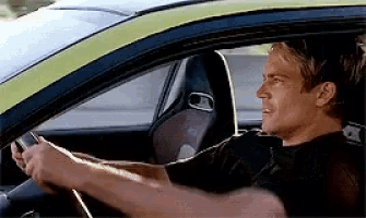 a man in a black shirt is driving a green car .