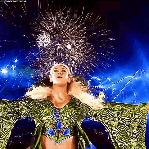 a woman in a green dress is standing in front of a fireworks display .
