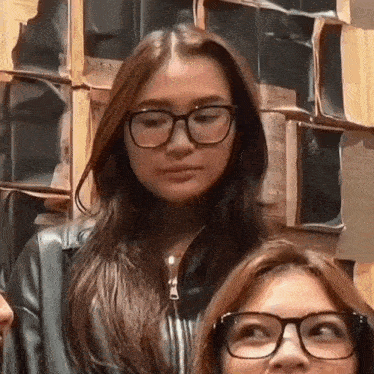a woman wearing glasses and a leather jacket is standing next to a woman wearing glasses .