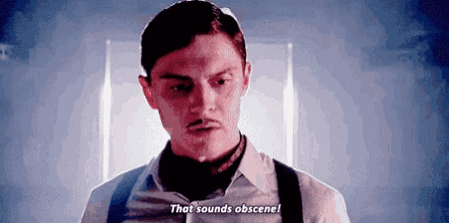 a man with a mustache and suspenders is standing in a dark room and talking .