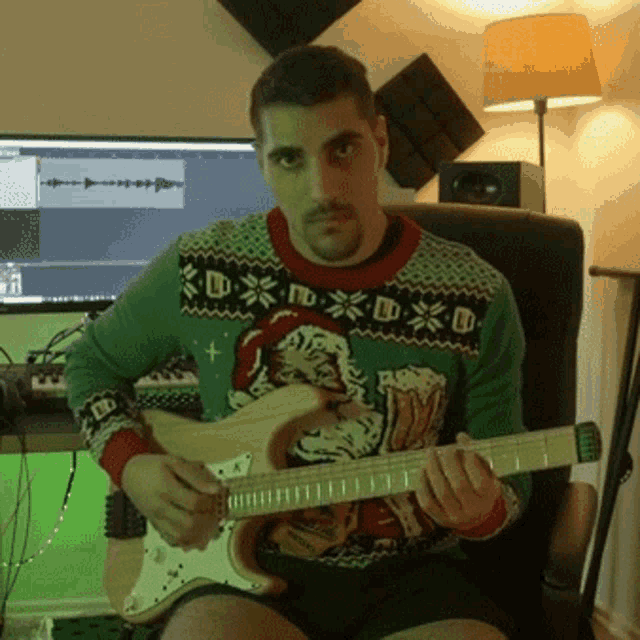 a man wearing an ugly christmas sweater holds a guitar