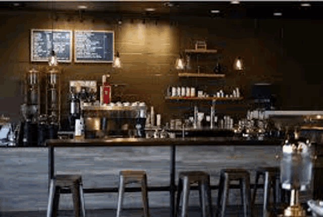 a coffee shop with a long counter and stools and a menu on the wall .