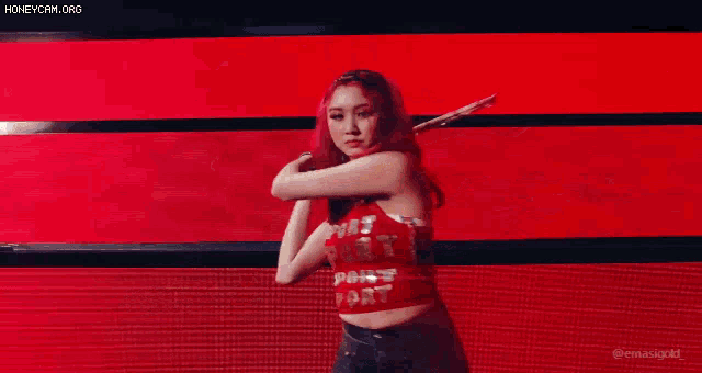 a woman in a red crop top is dancing on a stage with a light coming out of her hand .