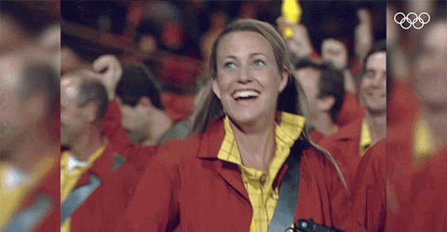 a woman in a red jacket is smiling in front of a group of people