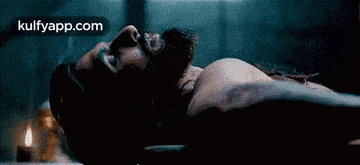 a man with a beard is laying on his back in a dark room with a candle in the background .