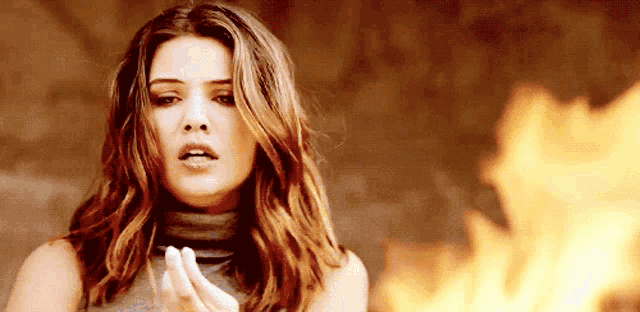 a woman is standing in front of a fire with her hands in the air .