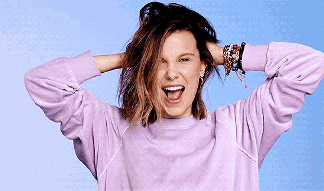 a woman wearing a purple sweater is holding her hair in her hands