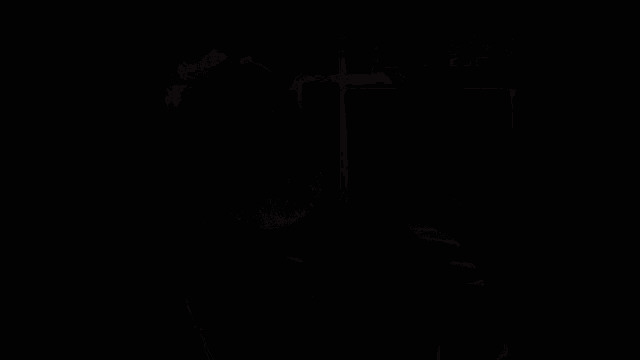 a man with a beard looks at the camera in front of a bookshelf