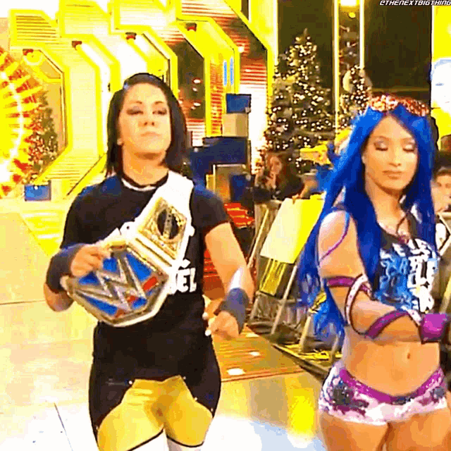 two female wrestlers are walking down the aisle holding their belts