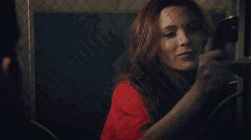 a woman in a red shirt is smiling in front of a fence