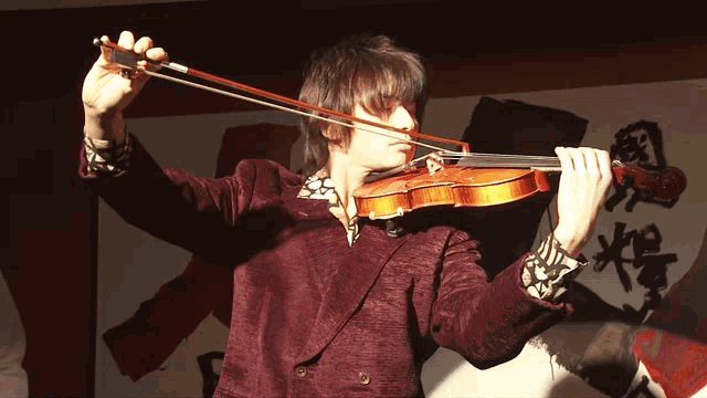 a man in a red jacket is playing a violin in front of chinese writing