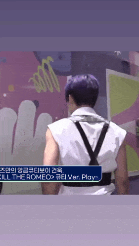 a man with purple hair is standing in front of a wall with graffiti on it