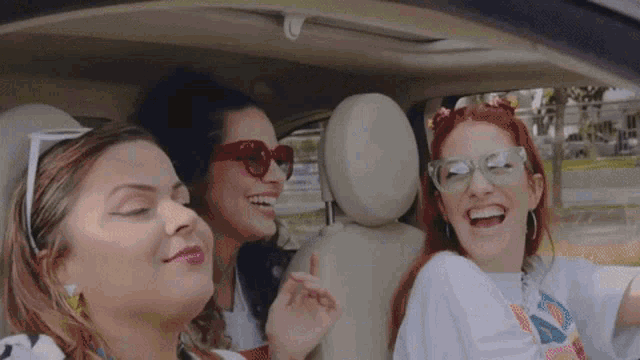 three women are sitting in the back seat of a car