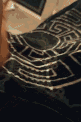 a person is laying on a bed with a black and white blanket with a greek key pattern .