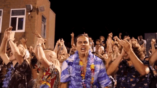 a man wearing a hawaiian shirt stands in front of a crowd