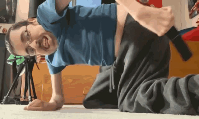 a man in a blue shirt and glasses is laying on the floor