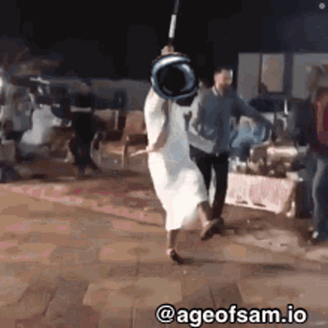 a woman in a white dress is holding a bucket over her head while a man stands behind her .