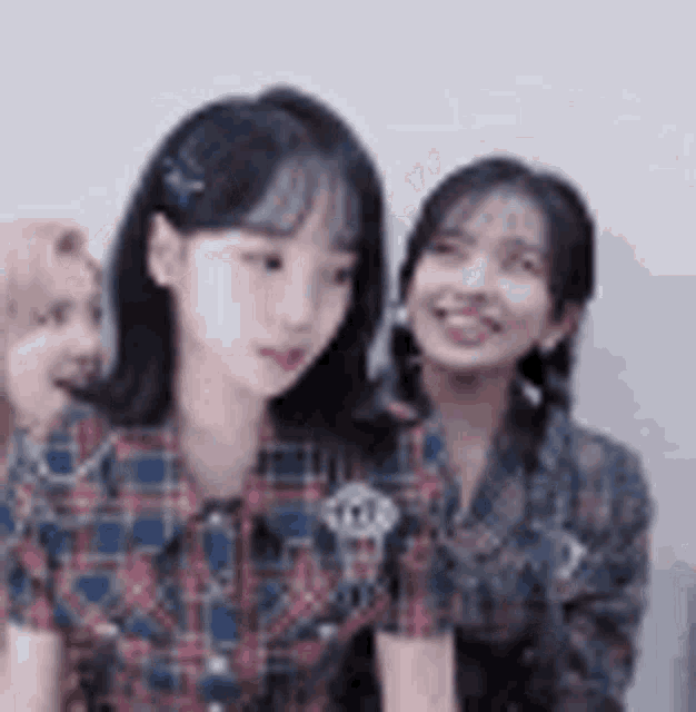 two girls are sitting next to each other and smiling . one of the girls is wearing a plaid shirt .