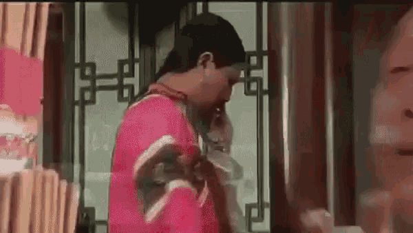 a man in a red shirt is standing next to a woman in a room and talking on a cell phone .