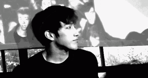 a black and white photo of a young man standing in front of a wall with a picture of a group of people on it .