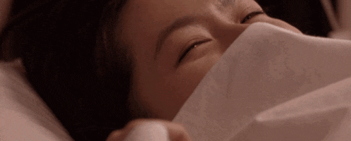a woman is laying in bed with her eyes closed and covering her mouth with a blanket .