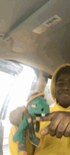 a man in a yellow hoodie is holding a stuffed dinosaur in his hand .