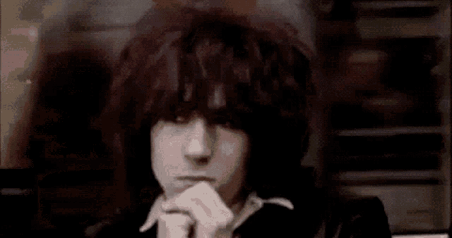 a close up of a person 's face with their hands on their chin and a blurry background .