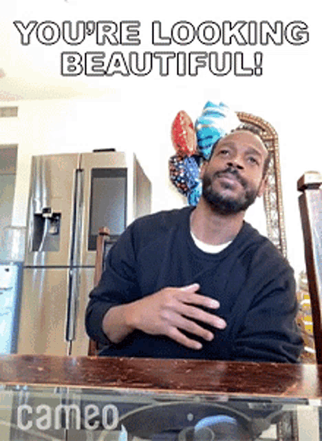 a man is sitting at a table with balloons behind him and the words you 're looking beautiful