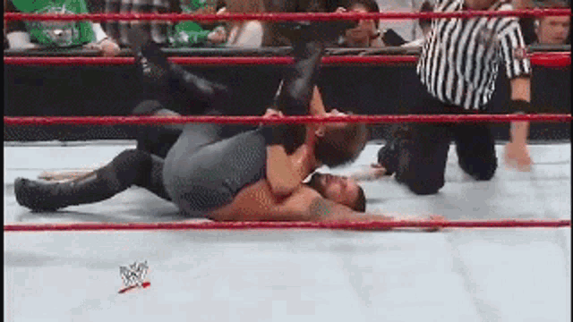two wrestlers are wrestling in a ring with a referee watching .