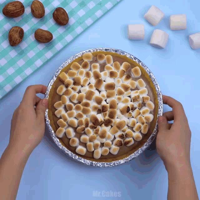 a person is holding a pie with marshmallows on top and the words mr.cakes written on the bottom