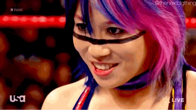 a woman with purple and blue hair is smiling and wearing a black mask .