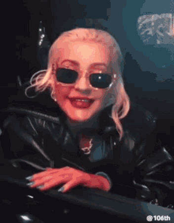 a woman wearing sunglasses and a leather jacket is sitting in a dark room .