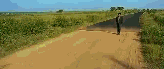 a man is walking down a dirt road in the countryside .