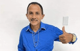 a man in a blue shirt is giving a thumbs up and holding a light switch .