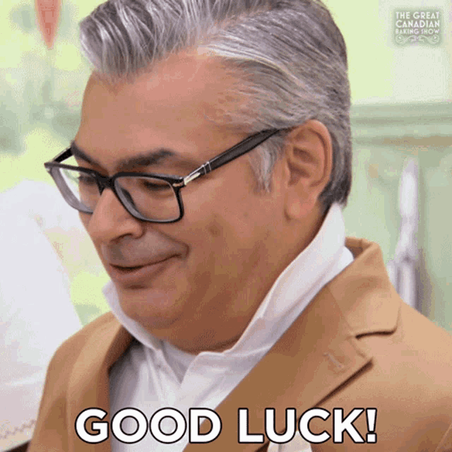 a man wearing glasses and a brown jacket is smiling and says good luck