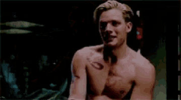 a shirtless man with a tattoo on his arm is smiling and looking at the camera .
