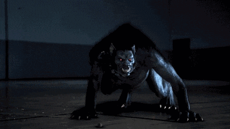 a werewolf with red eyes is crawling on the floor in the dark .