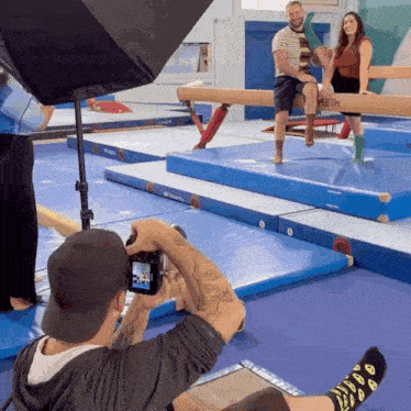 a man is taking a picture of a woman on a balance beam in a gym
