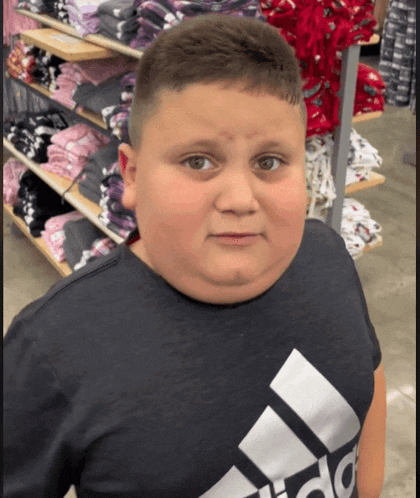 a boy wearing a black adidas shirt stands in a store