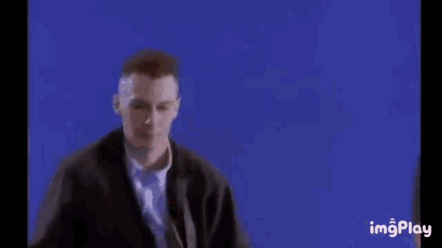 a group of men are standing next to each other in front of a blue background . one of the men is playing a guitar .