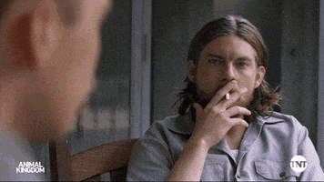 a man is smoking a cigarette while sitting in a chair in front of another man .