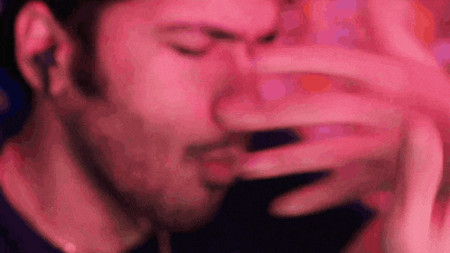 a close up of a man covering his face with his hand in a pink light .